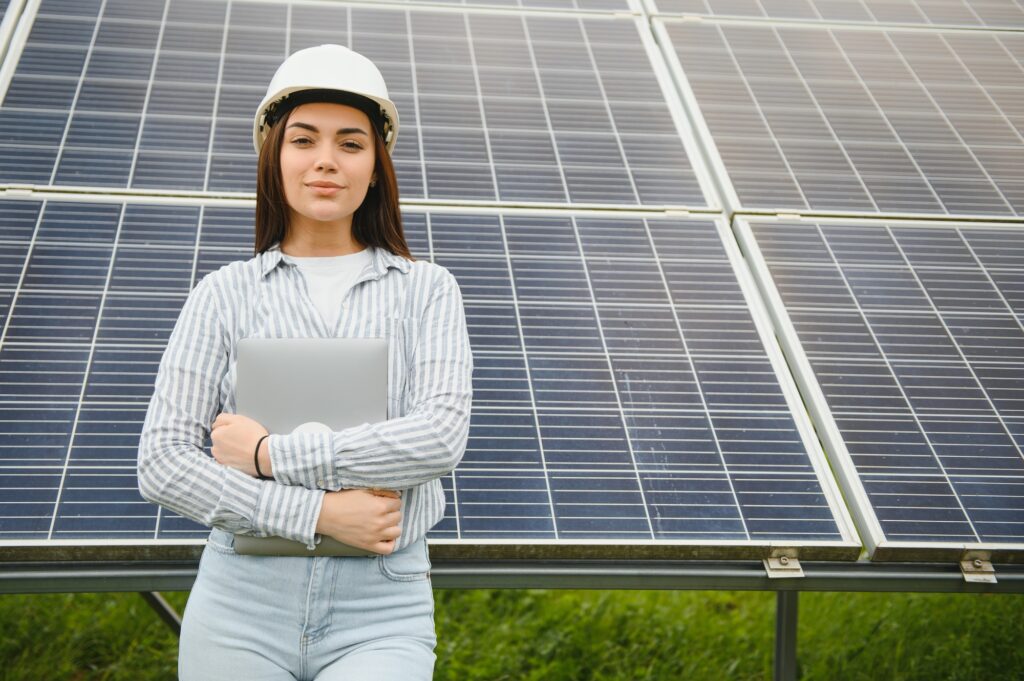 Portrait of beautiful female engineer technologist standing among solar panels